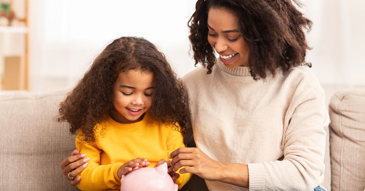 Mom and daughter smiling looking at piggy bank.