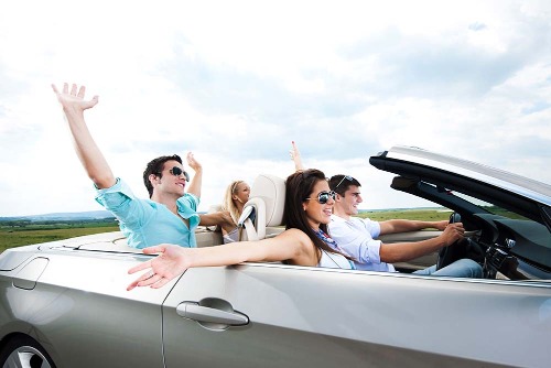 couples in a convertible putting their hands in the air on a partly sunny day