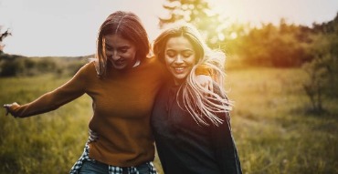 Two women with arms around each other walking in field