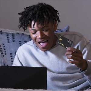 Happy young black man holding gold debit card while online shopping. 