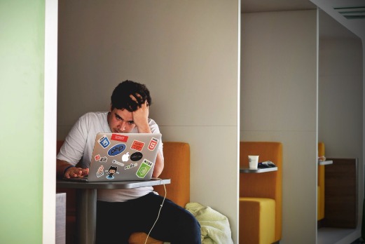 man sitting in front of a sticker-covered laptop