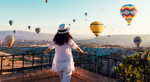 Woman standing on balcony overlooking the desert and hot air balloons