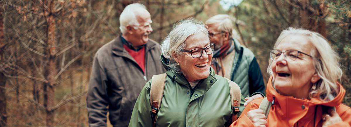 Elder group of men and women smiling and laughing while hiking in the woods.