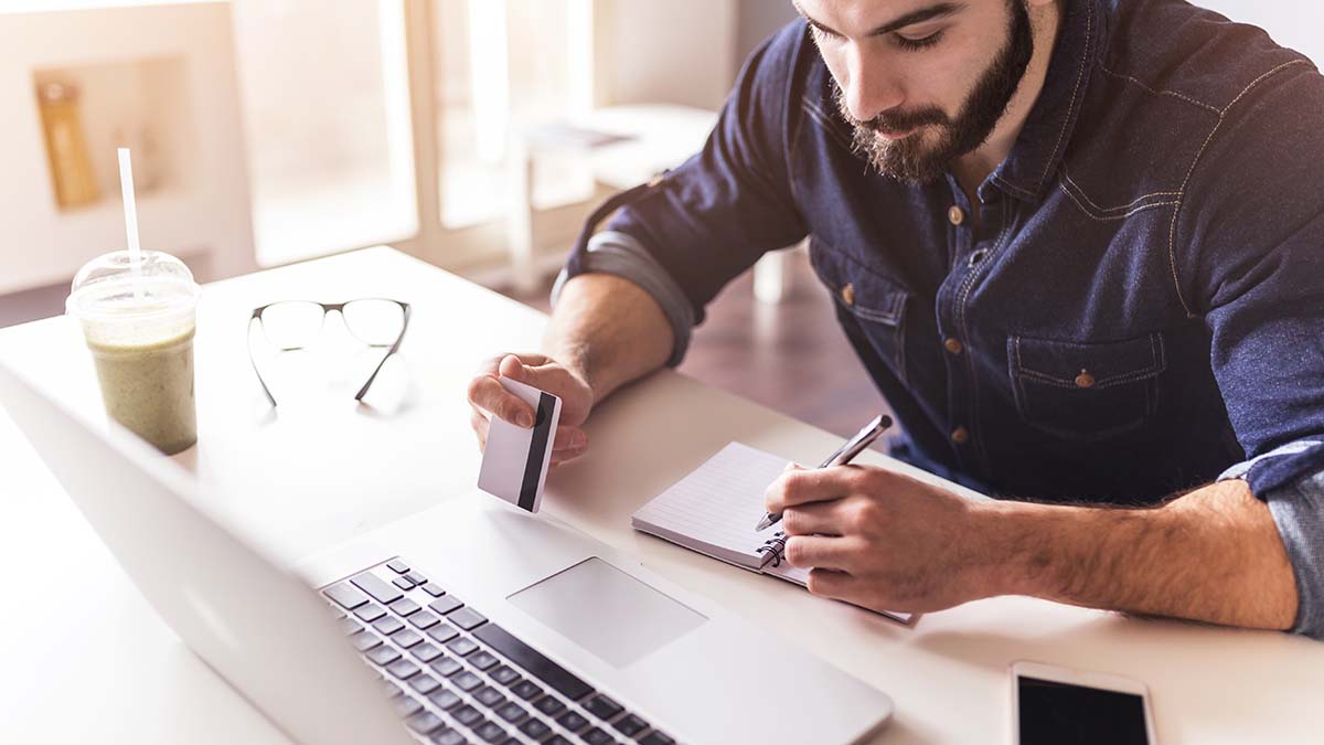 man sitting in front of laptop computer with debit card