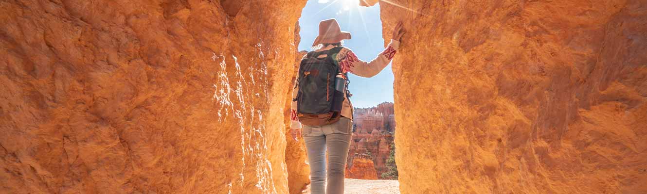 Person hiking thru a rock opening, back is to us with a hat on.