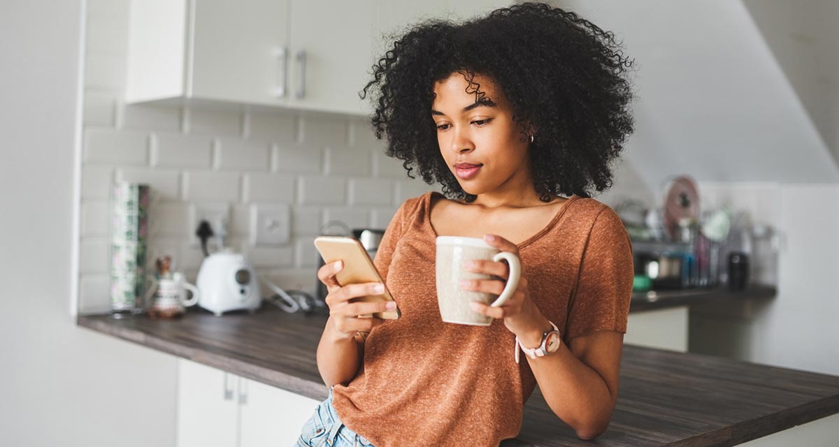 Shot of a young woman using a smartphone and having coffee in the kitchen at home