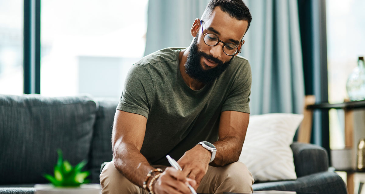 Man sitting on a couch writing out a check.