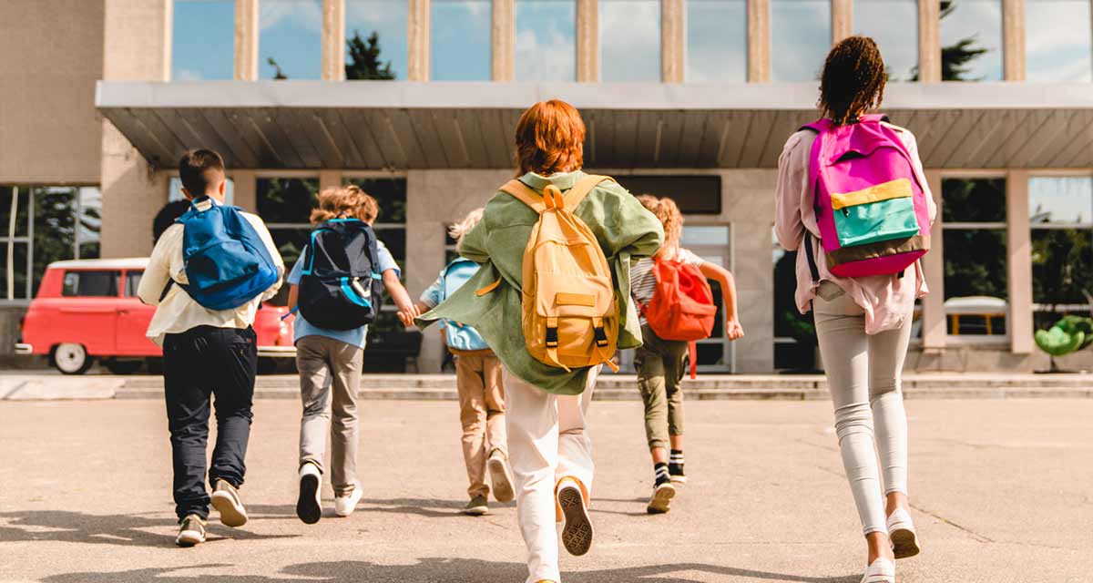 children running towards a school building with vibrant backpacks on.