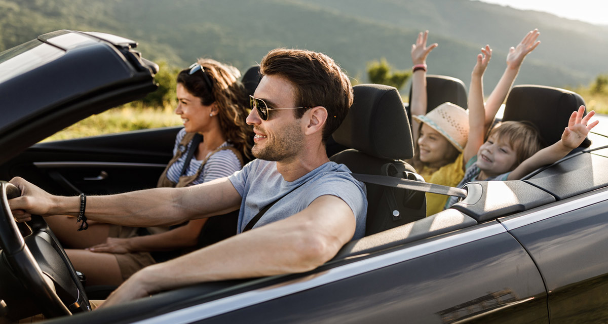 Happy parents and their small kids going on road trip in convertible car.