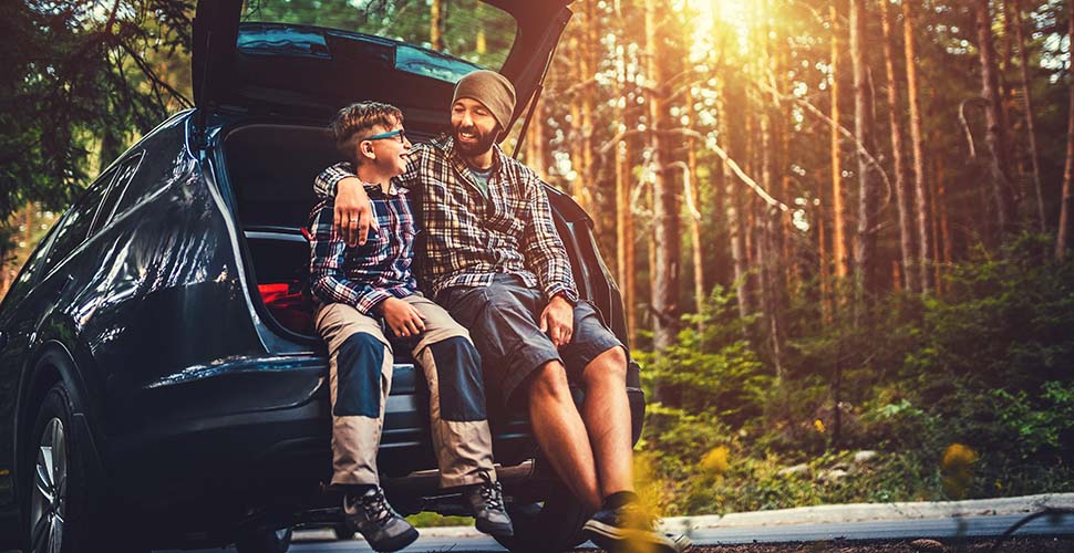 Father and son sitting on a car tailgate in the woods