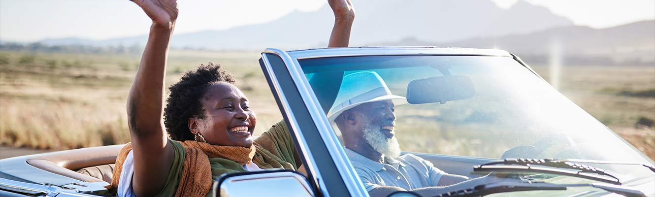 older black couple driving in a scenic road in a classic sports car.