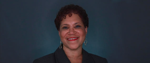 Carolyn Jordan in front of a backdrop looking at camera and smiling.