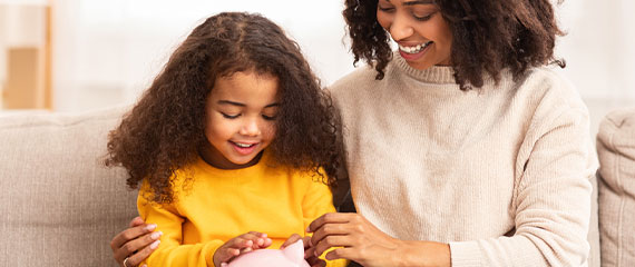 Mom and daughter smiling looking at piggy bank.