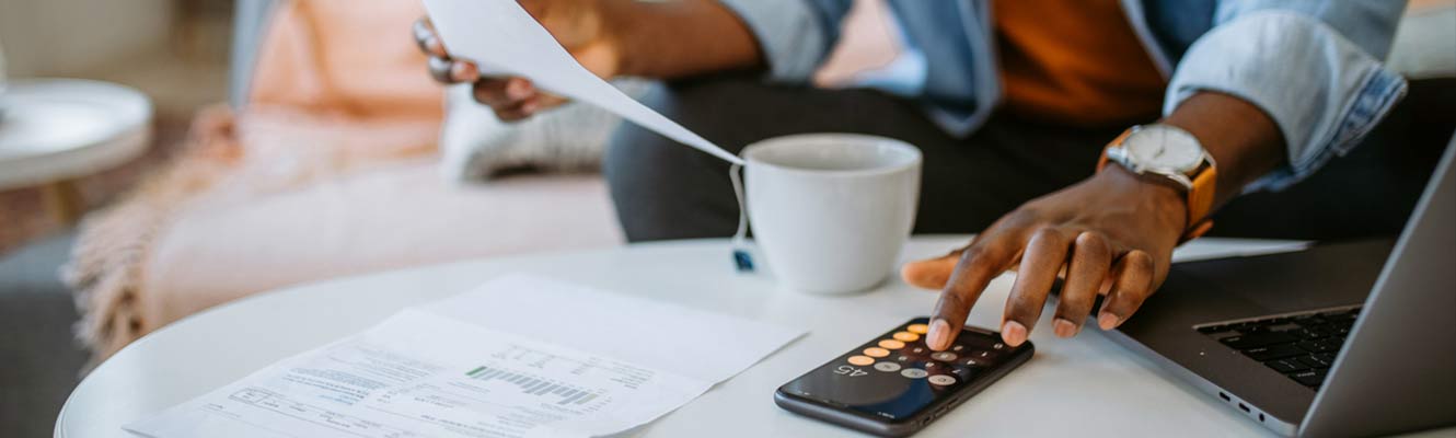 Young black man at home, sitting in sofa, checking financial documents, going through finances, paying bills online and planning investments.