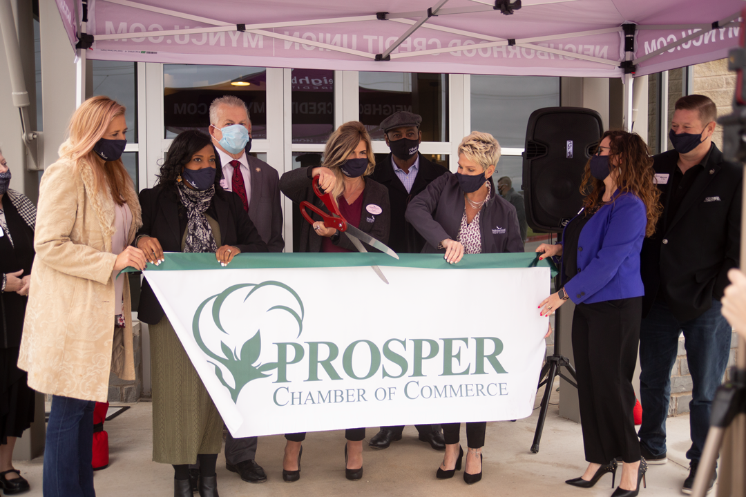 people surrounding banner and ribbon to cut in honor of a grand opening celebration