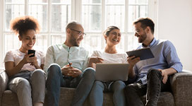 Four people sitting on a couch with books, phone, and laptop. Interacting and laughing with one another.