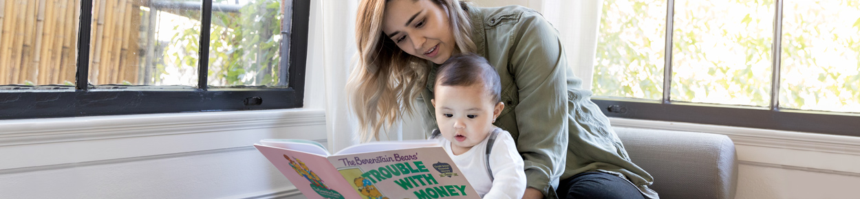 A  mother sitting in the corner reading a book to her young child