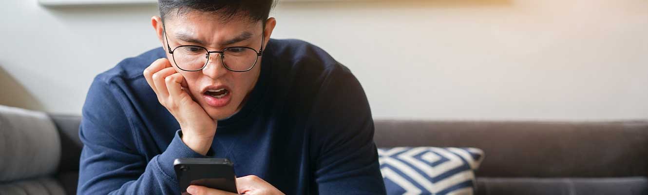 Young man looking down at his phone in a shocked look 