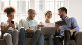 Four people sitting on a couch with books, phone, and laptop. Interacting and laughing with one another.