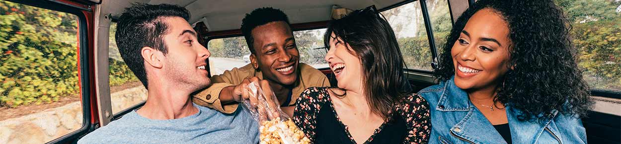 Group of College friends having fun in the back of a van. smiling and laughing at one another.