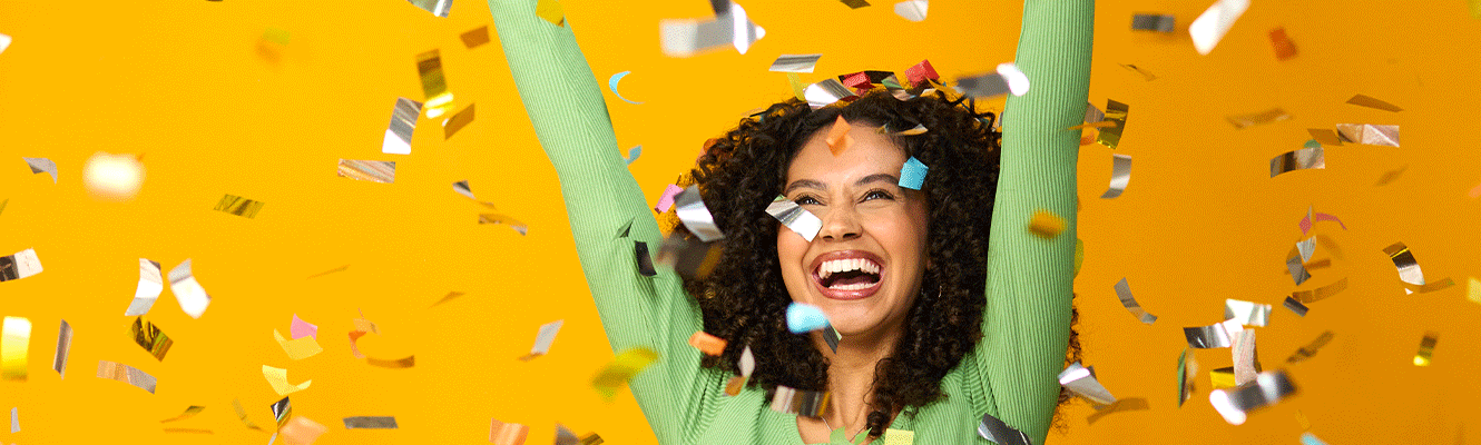 Studio Shot Of Excited Woman Celebrating Big Win Showered In Tinsel Confetti On Yellow Background