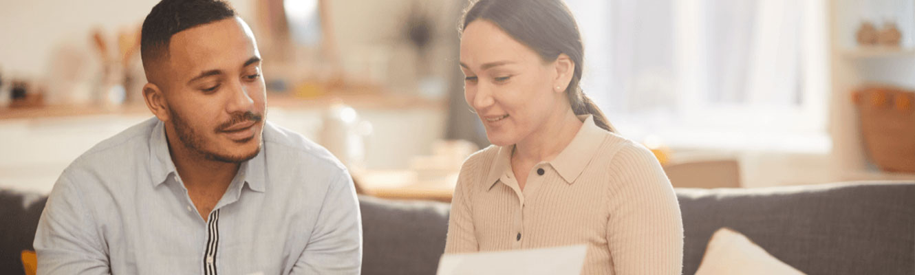 man and woman sitting at home looking over a paper 