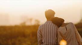 Young couple looking off into a wooded area at dusk. Female is leaning head on males shoulder