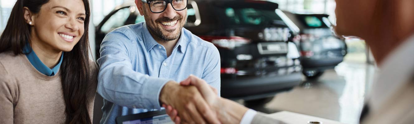 Young happy couple came to a successful agreement with car salesman during a meeting in a showroom.