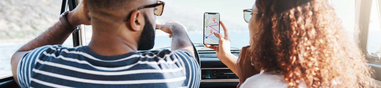 A couple in the front seat of the car looking at maps on a cell phone