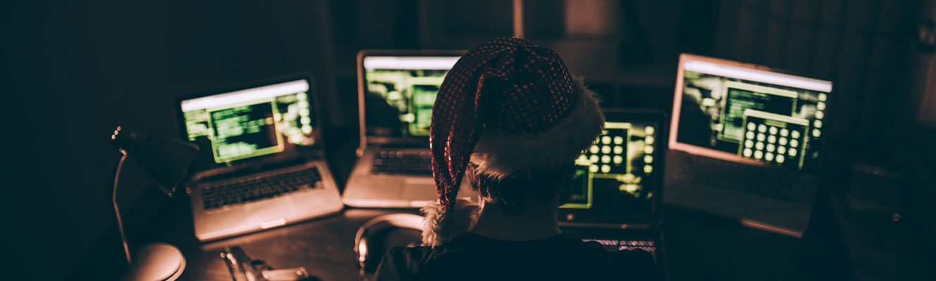 Computer hacker wearing santa hat while working on laptop late at night
