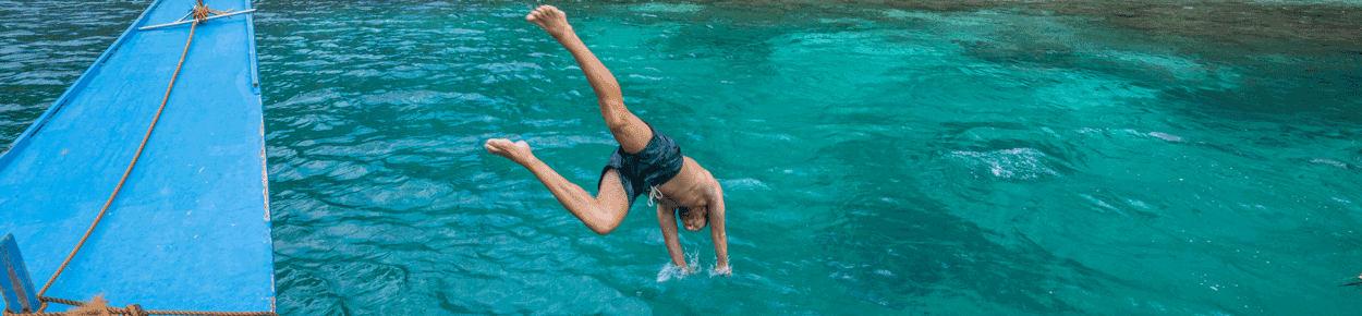 man diving into ocean next to blue boat