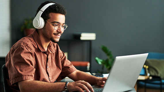 Young man wearing headphones and looking down at his laptop reading something on the screen