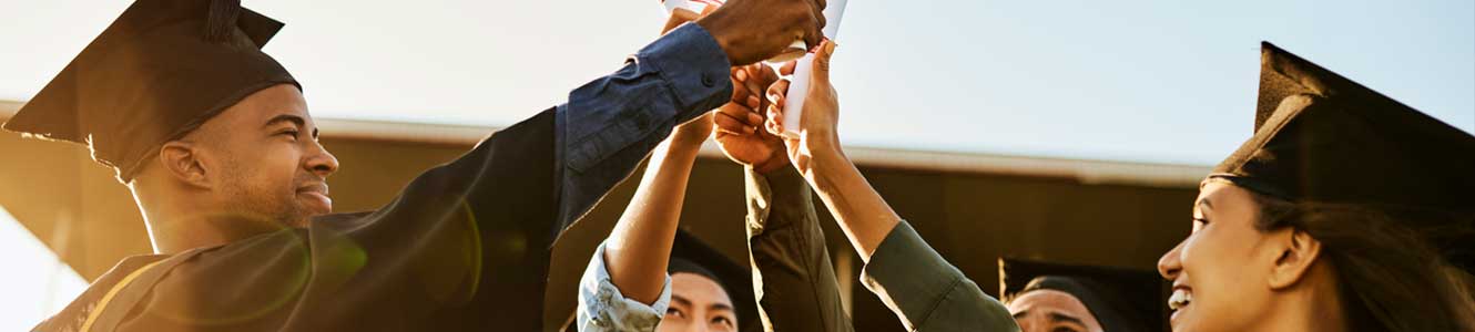 A group of young adults in cap and gowns holding diplomas up in the air