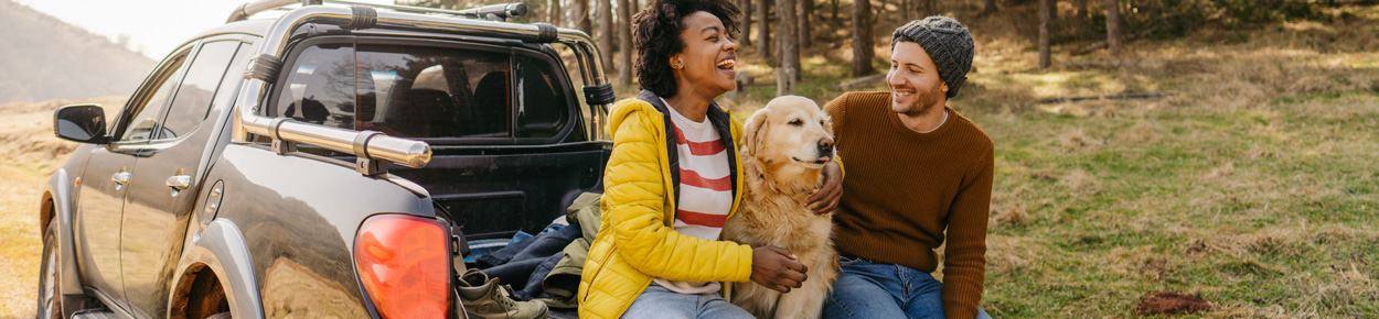 Smiling couple sitting on truck tailgate with their dog