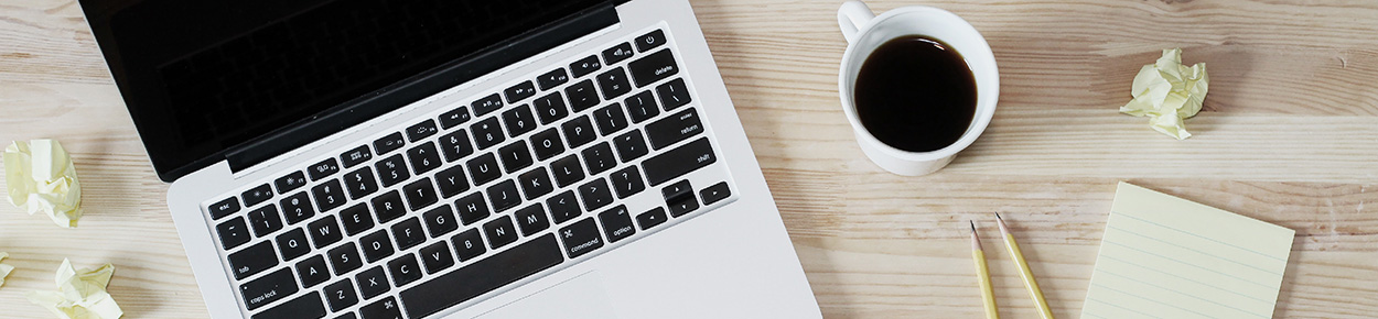 Laptop computer on a desk with coffee and notepad