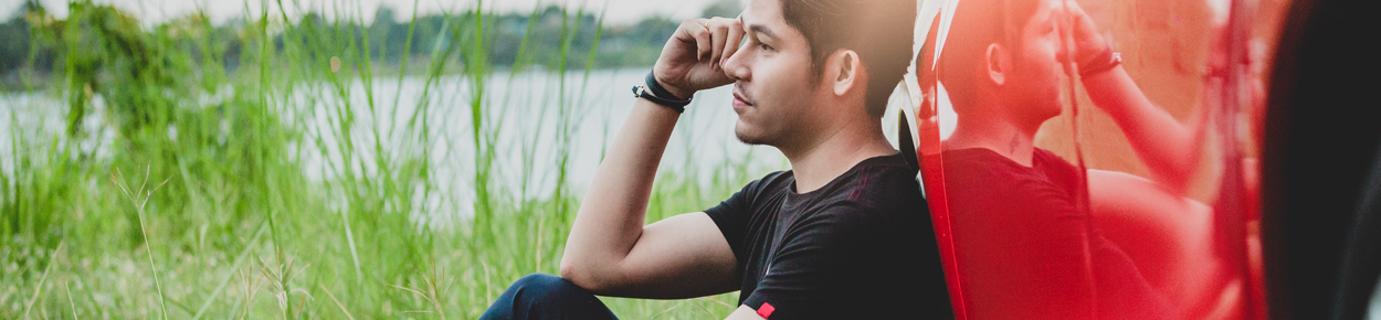 man next to lake leaning against his red vehicle