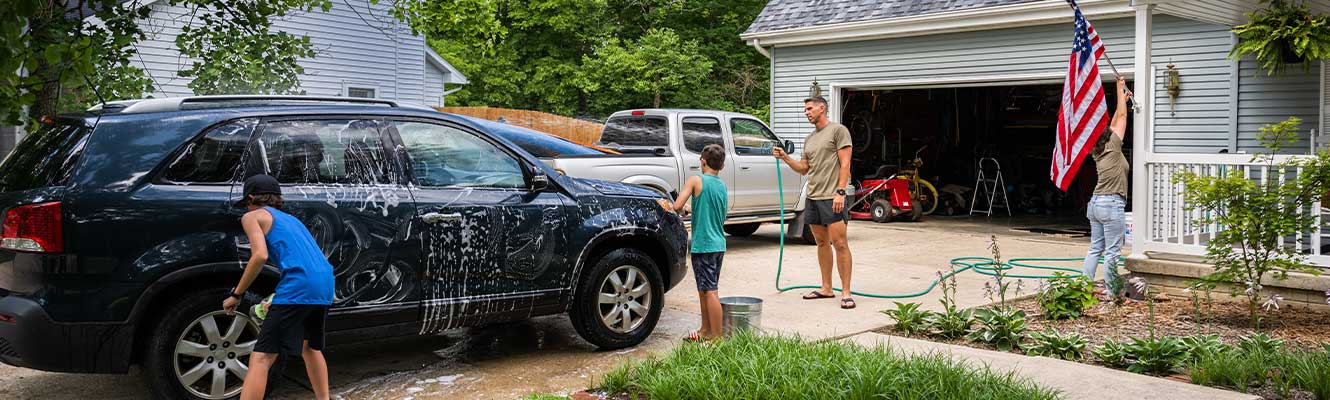 A family of four (Dad, Mom, and two sons) in their driveway washing a car.