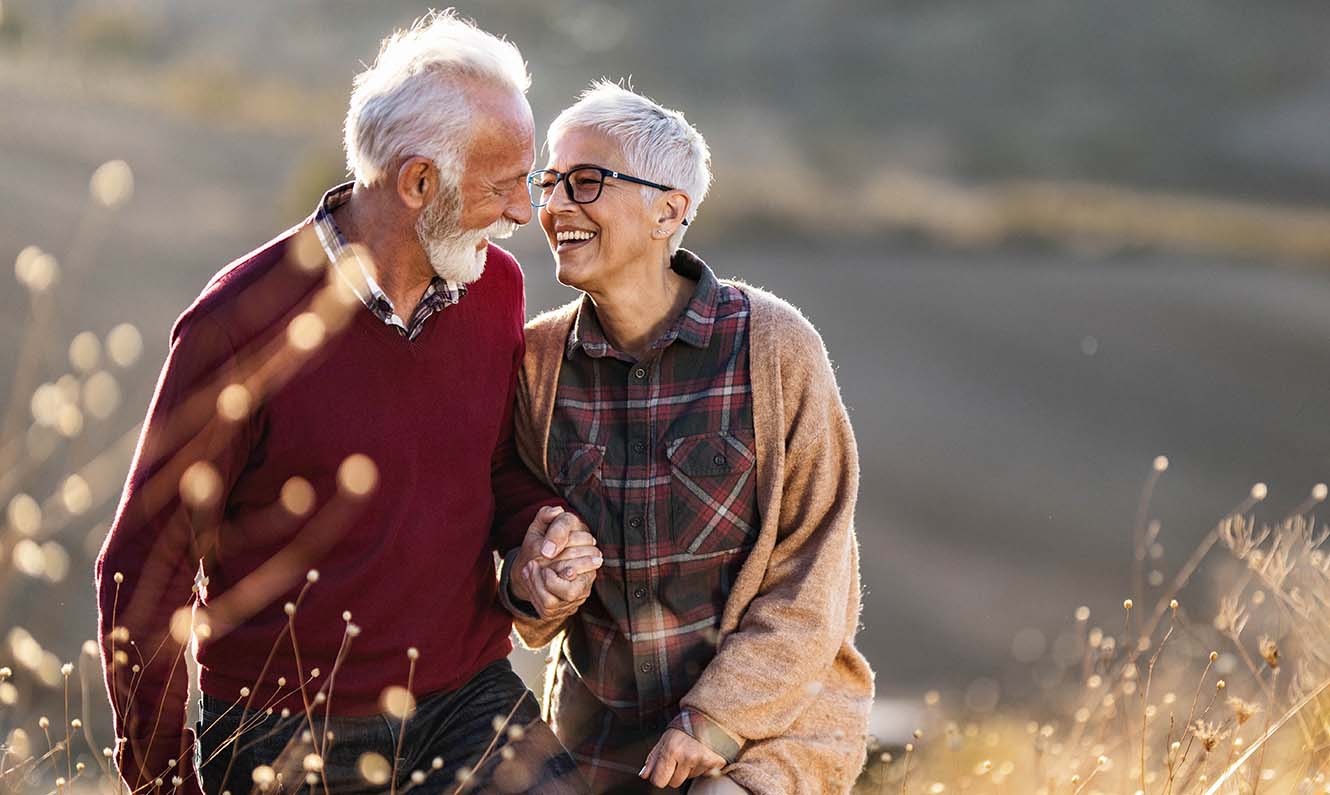 Older couple holding hands in a field smiling