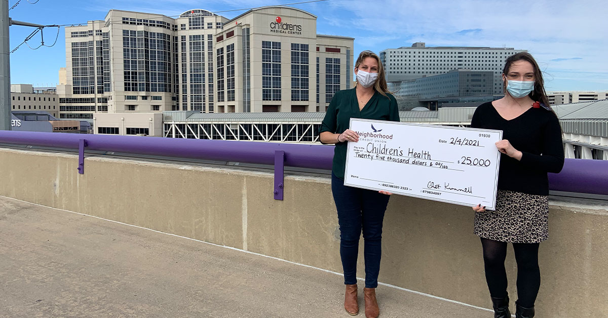 Still image of two women holding a large check in front of Children's Medical Center
