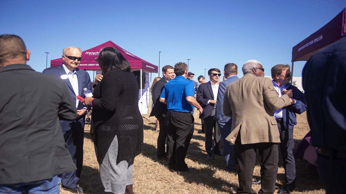 Crowd of people standing in a lot socialize and shaking hands.