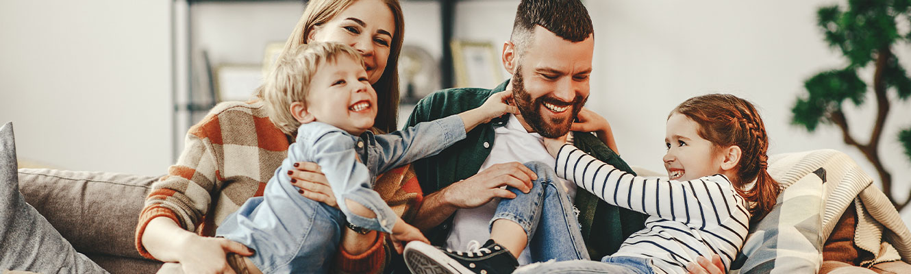 A mother and father laughing and playing with their children on a couch