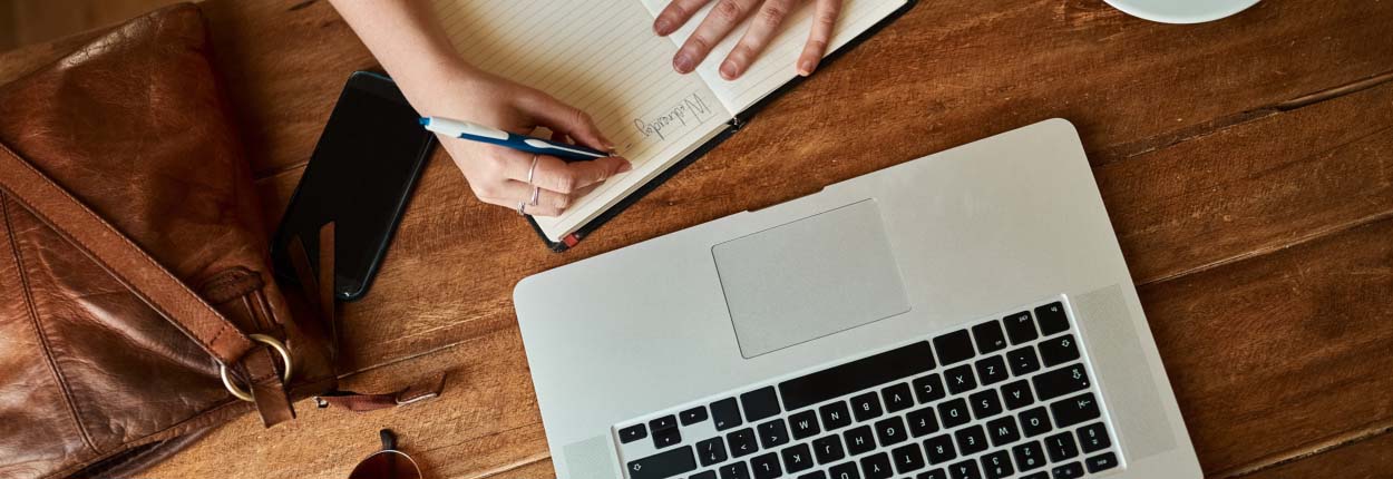 Woman writing in journal next to bag and laptop