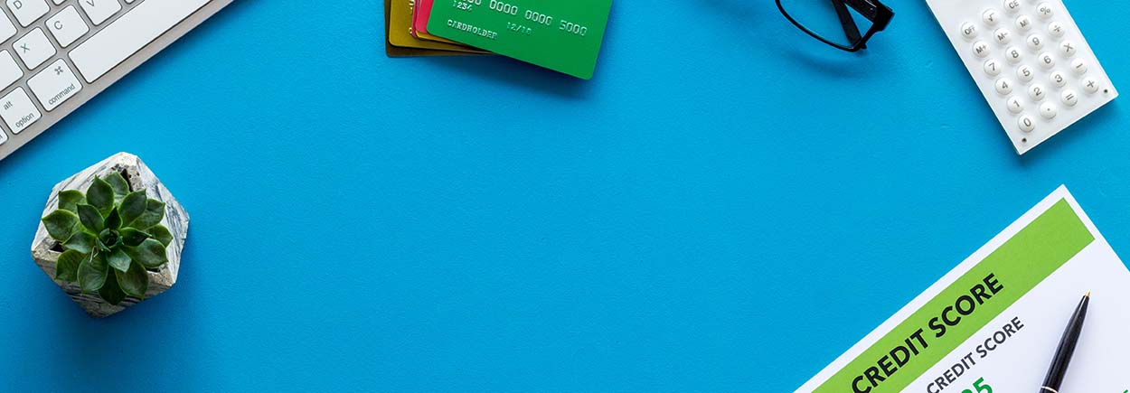 Blue desk with credit cards, plant, paper, and glasses next to a keyboard