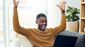 Shot of a young man cheering while using a laptop at home