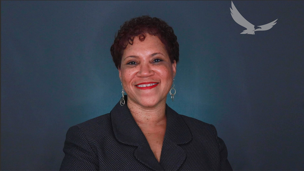 Carolyn Jordan in front of a backdrop looking at camera and smiling.