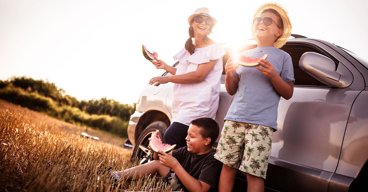 image of a mom and two children eating watermelon and laughing outside of their car